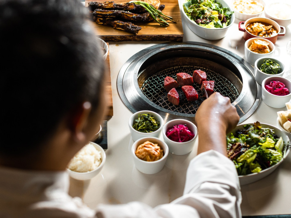 chef preparing korean barbecue feast surrounded by side dishes